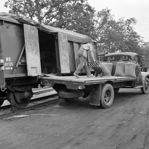 846599 Afbeelding van het overladen van zakken van een goederenwagen van N.S. naar een vrachtauto te Peize (?) (aan de ...